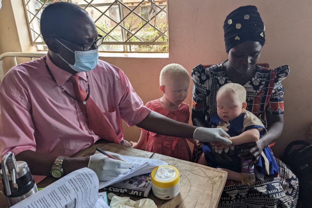 Un trabajador sanitario local ofrece con dedicación información y atención dermatológica a dos niños con albinismo, cuidando su salud.